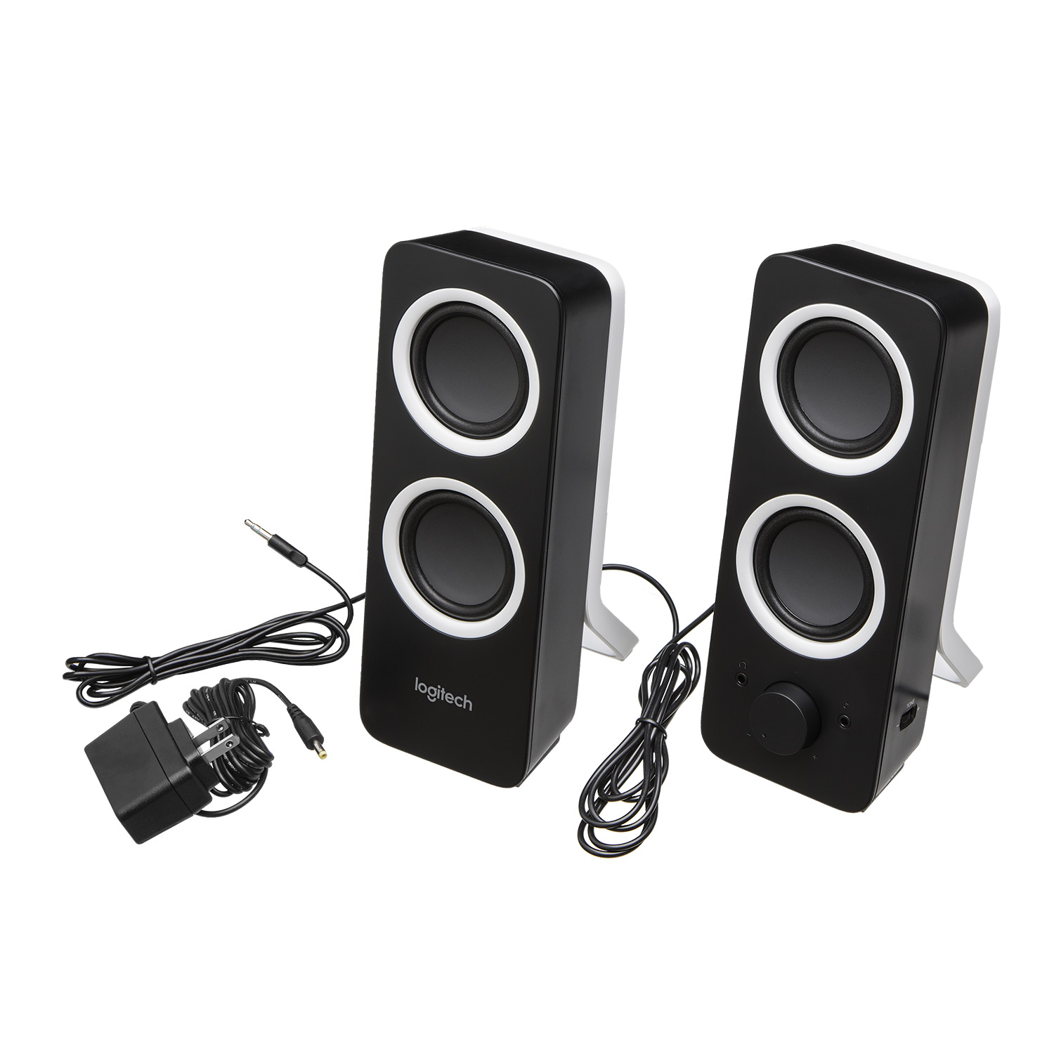 Dos altavoces negros con anillos blancos, verticales. Cables y adaptador de corriente también visibles.