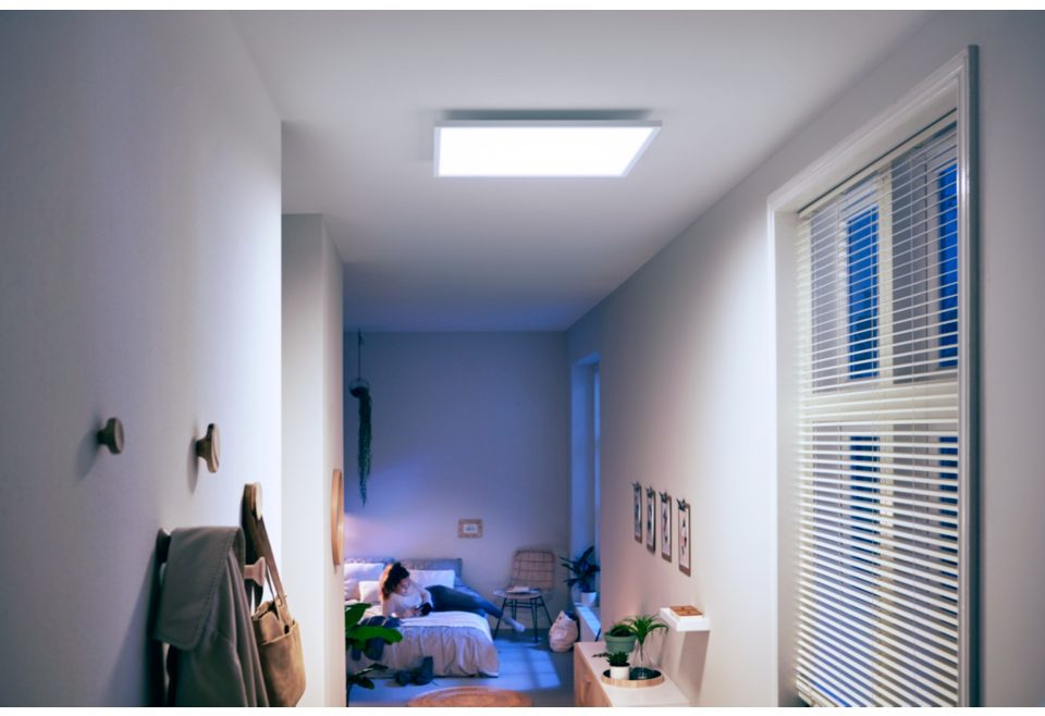 Een gang met een vrouw in bed in een kamer, een plafondlamp en een raam rechts.