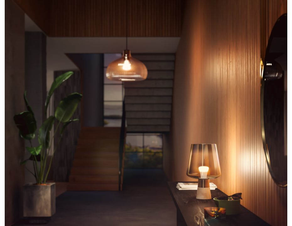 A hallway with a lamp on a dark table. There is a plant in a pot and a set of stairs.