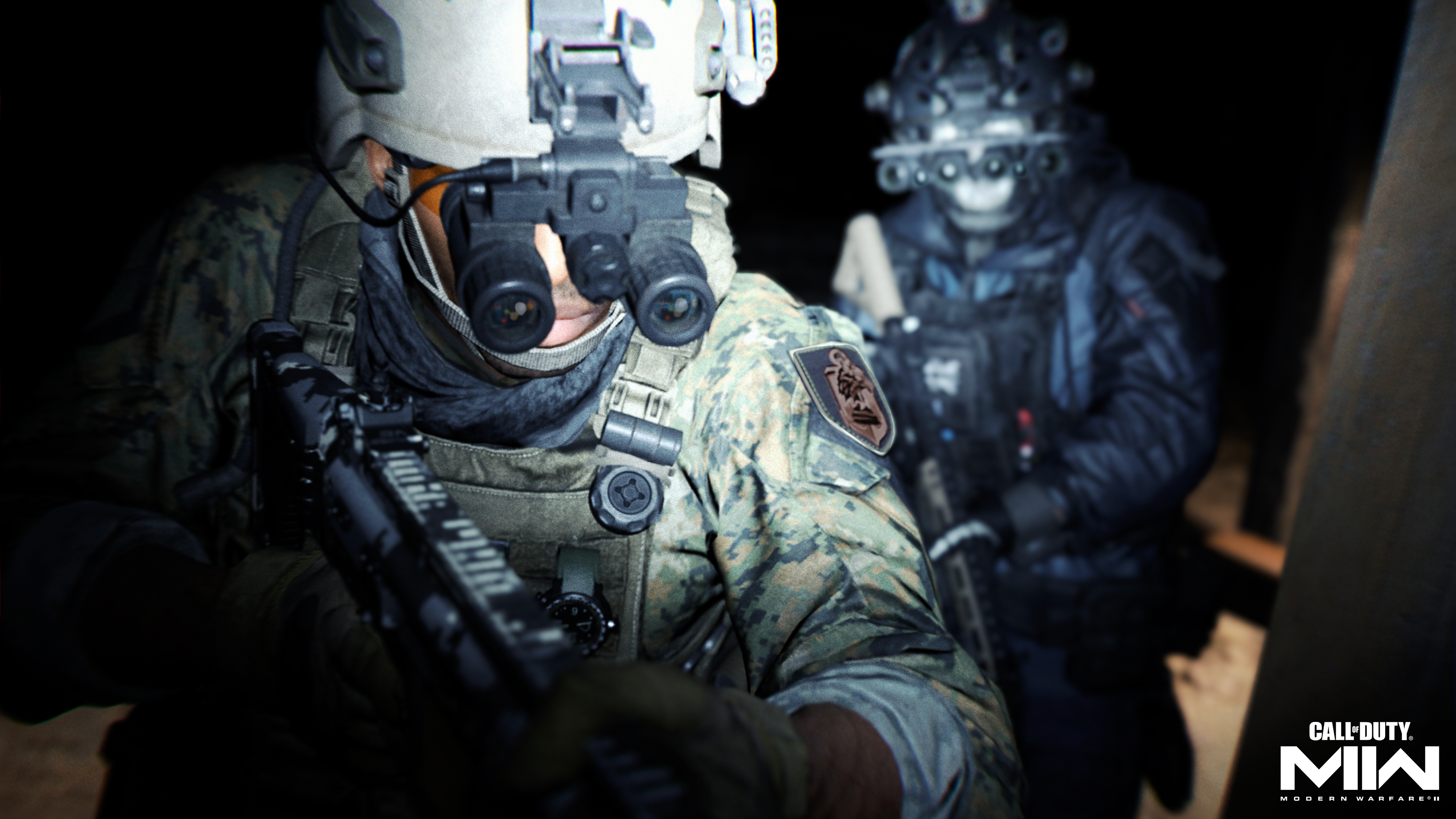 Zwei Soldaten in Taktik-Ausrüstung und Nachtsichtgeräten halten Gewehre in einem dunklen Raum.