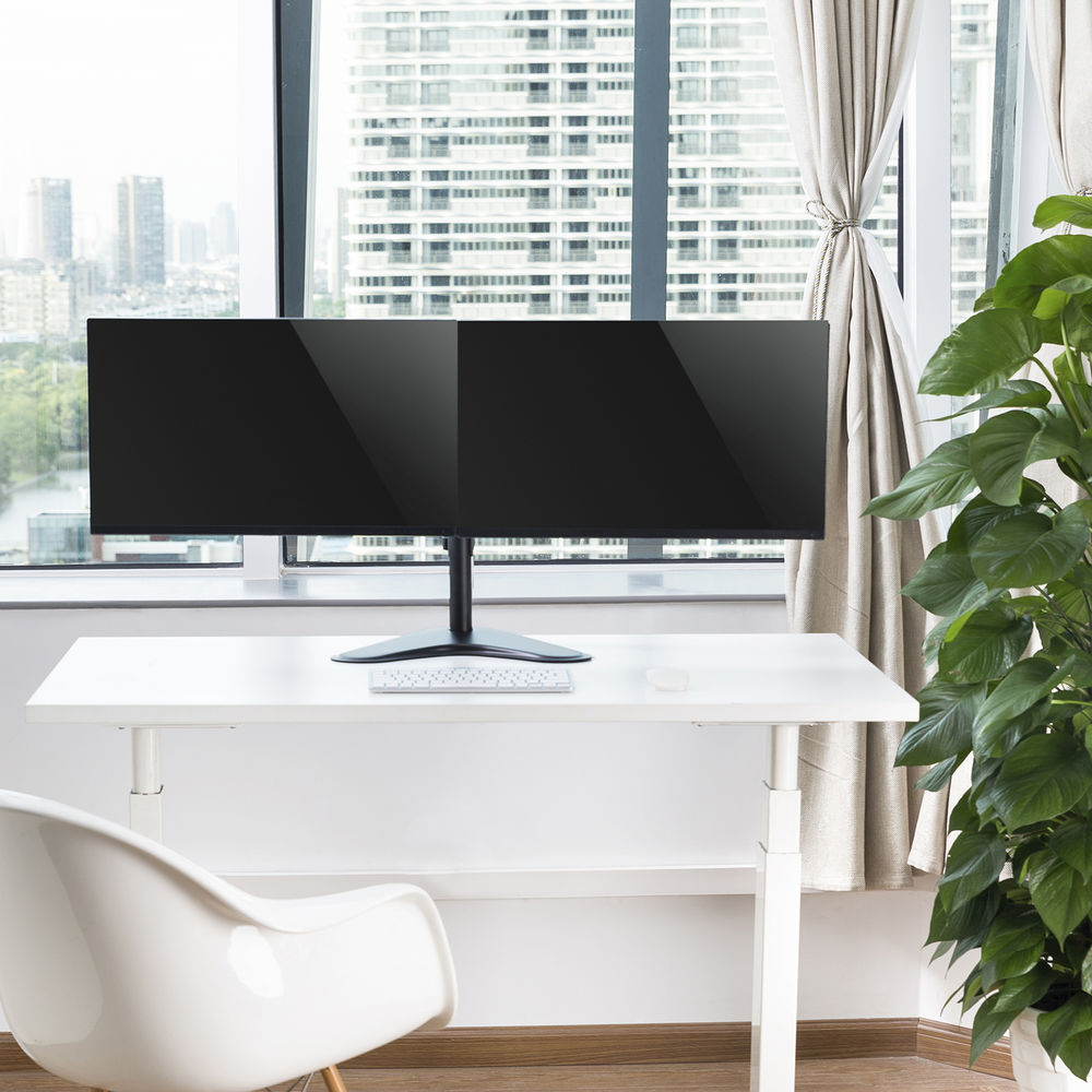 A wide monitor on a desk with a keyboard. A window and plant are in the background.