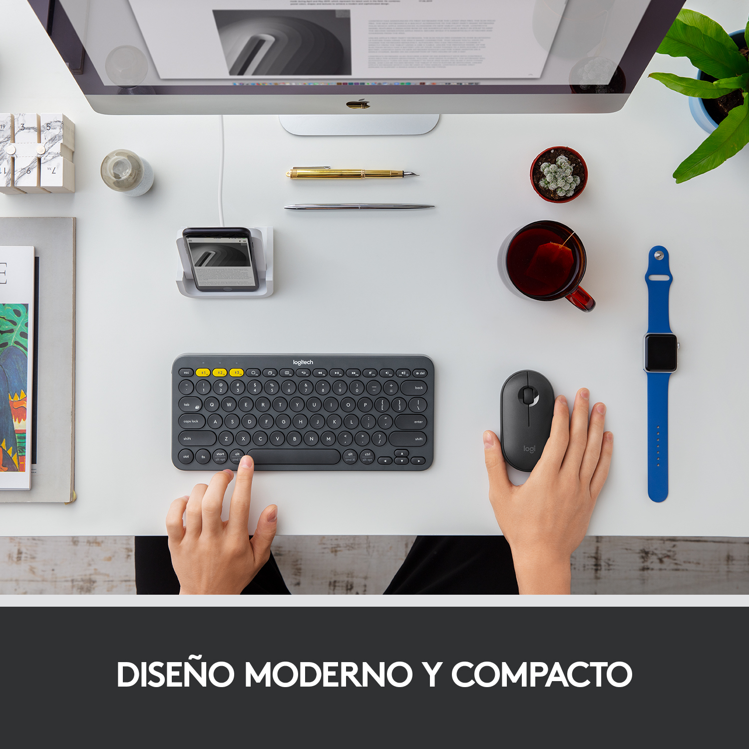 Escritorio con teclado, ratón, monitor, bolígrafo, taza, reloj y planta sobre superficie blanca.