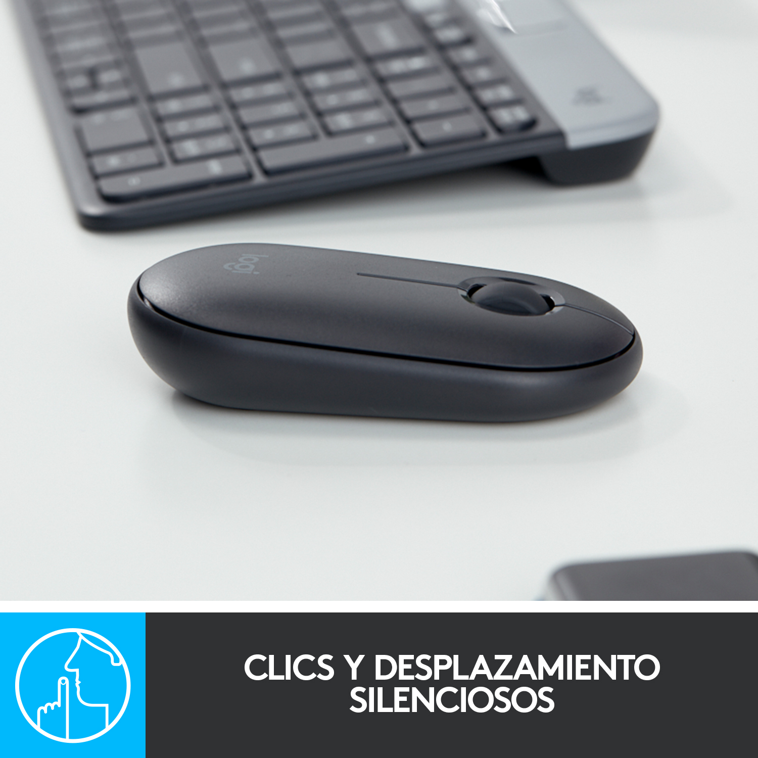 Ratón Logitech negro sobre superficie blanca, con teclado parcialmente visible.