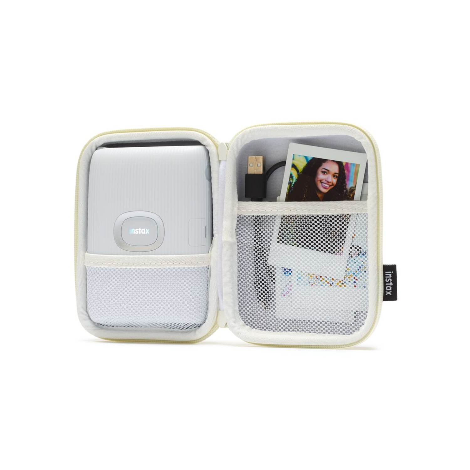 Witte Instax camerahoes, open. Camera, foto's en USB-kabel binnenin. Witte achtergrond.