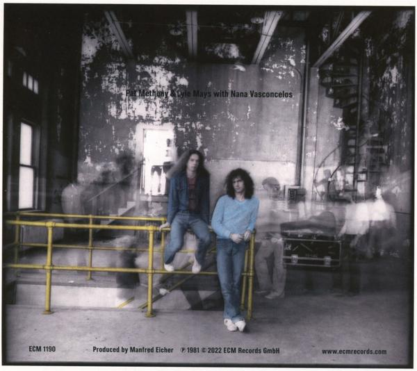 Albumcover mit zwei Männern an einem gelben Geländer und einem verschwommenen Hintergrund.