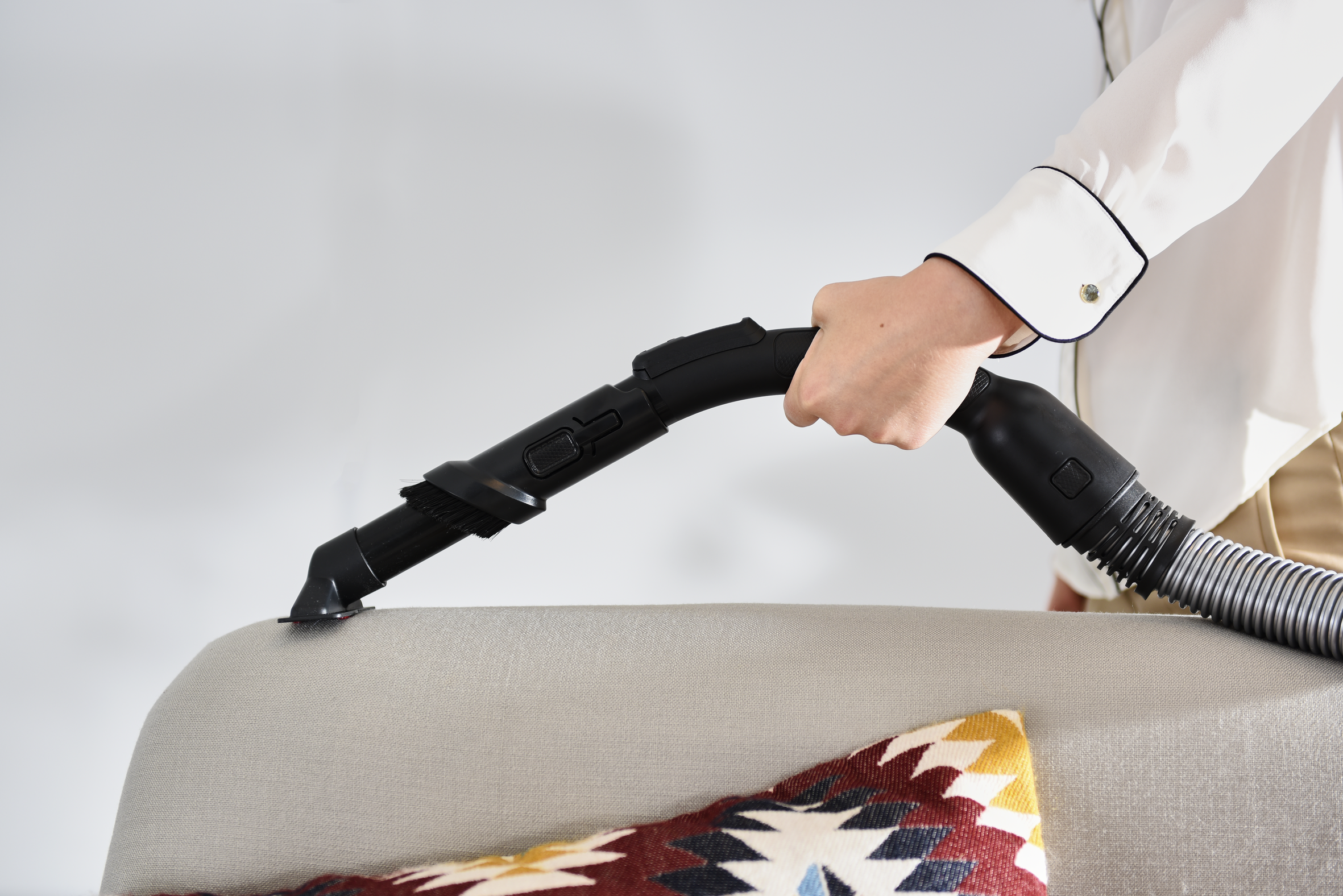 Una persona aspirando el brazo de un sofá con una aspiradora de mano.