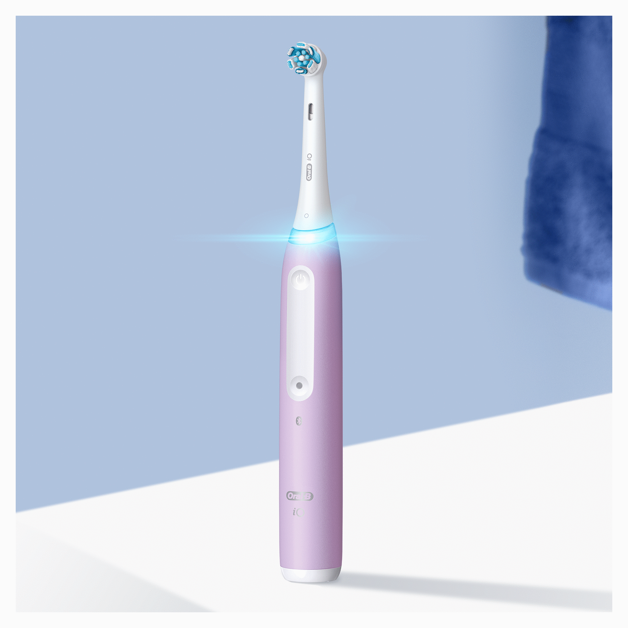 Pink electric toothbrush, blue light, white handle and brush head.  Blue background with a towel.