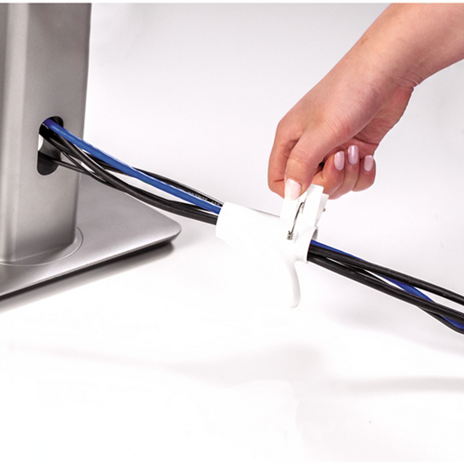 Una mano organizando cables con un organizador blanco sobre una superficie blanca.