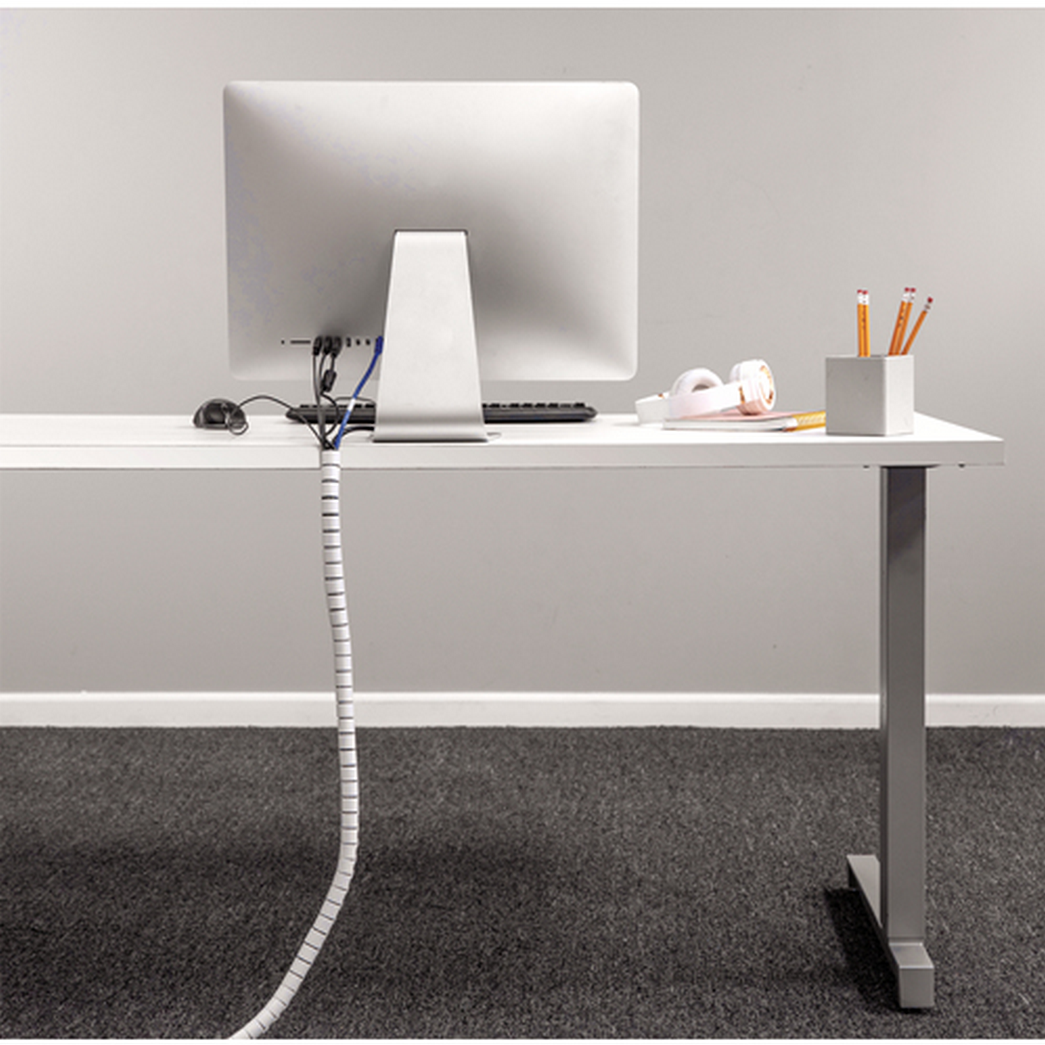 Un escritorio blanco con un monitor de computadora y un organizador de cables, con una alfombra gris.