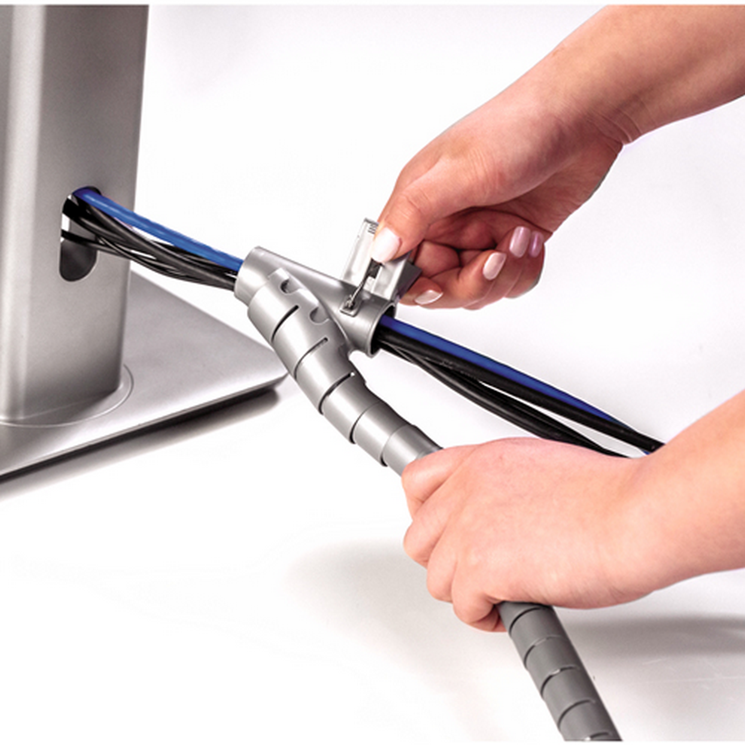 Manos usando un organizador de cables gris para gestionar cables conectados a una torre de ordenador plateada.