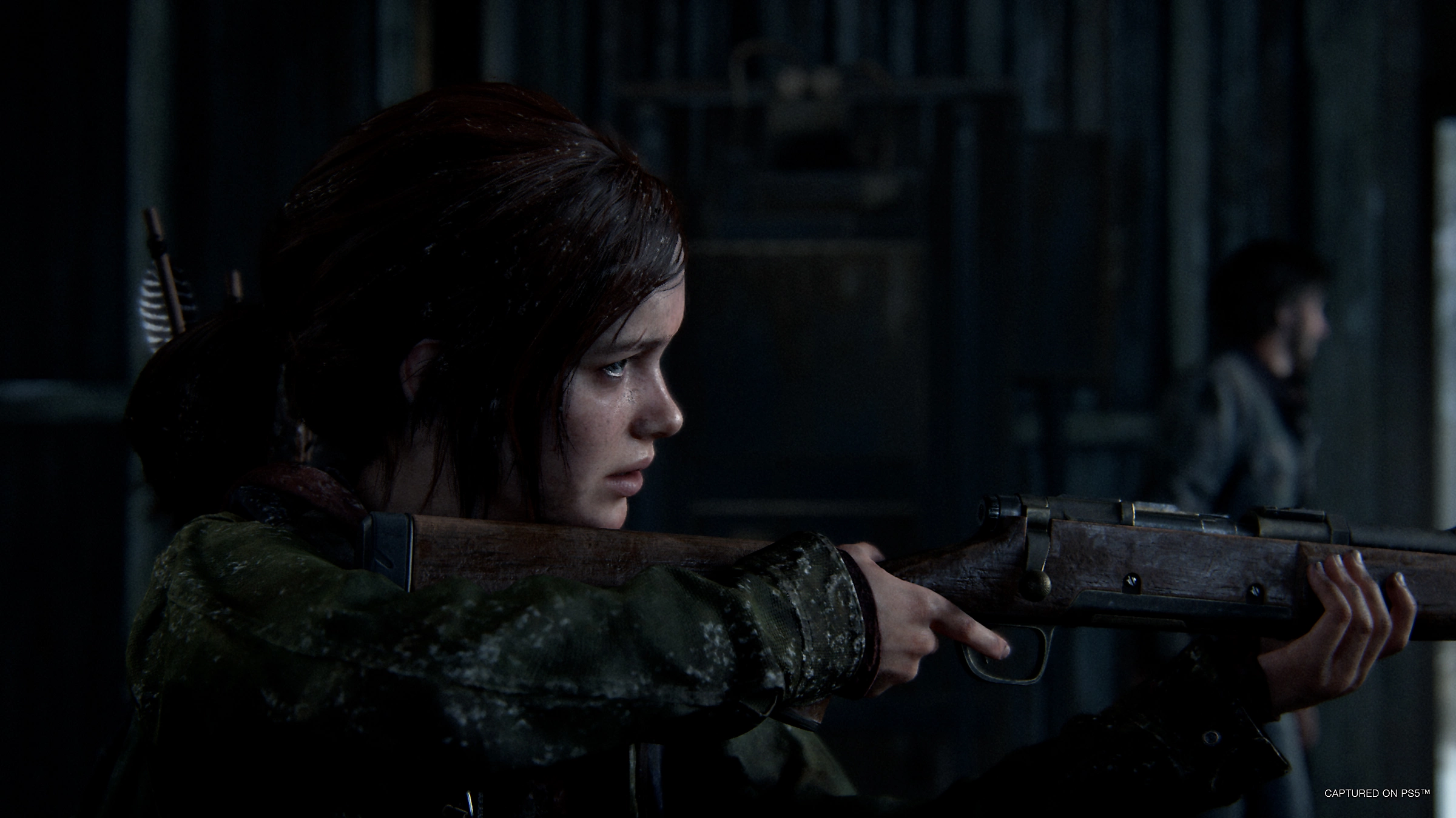 Una donna che mira con un fucile in un ambiente interno buio. Il logo di The Last of Us è nell'angolo.