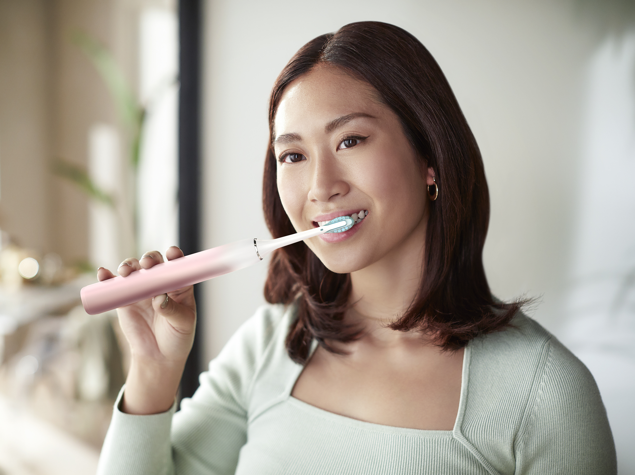 Une femme se brossant les dents avec une brosse à dents électrique rose.