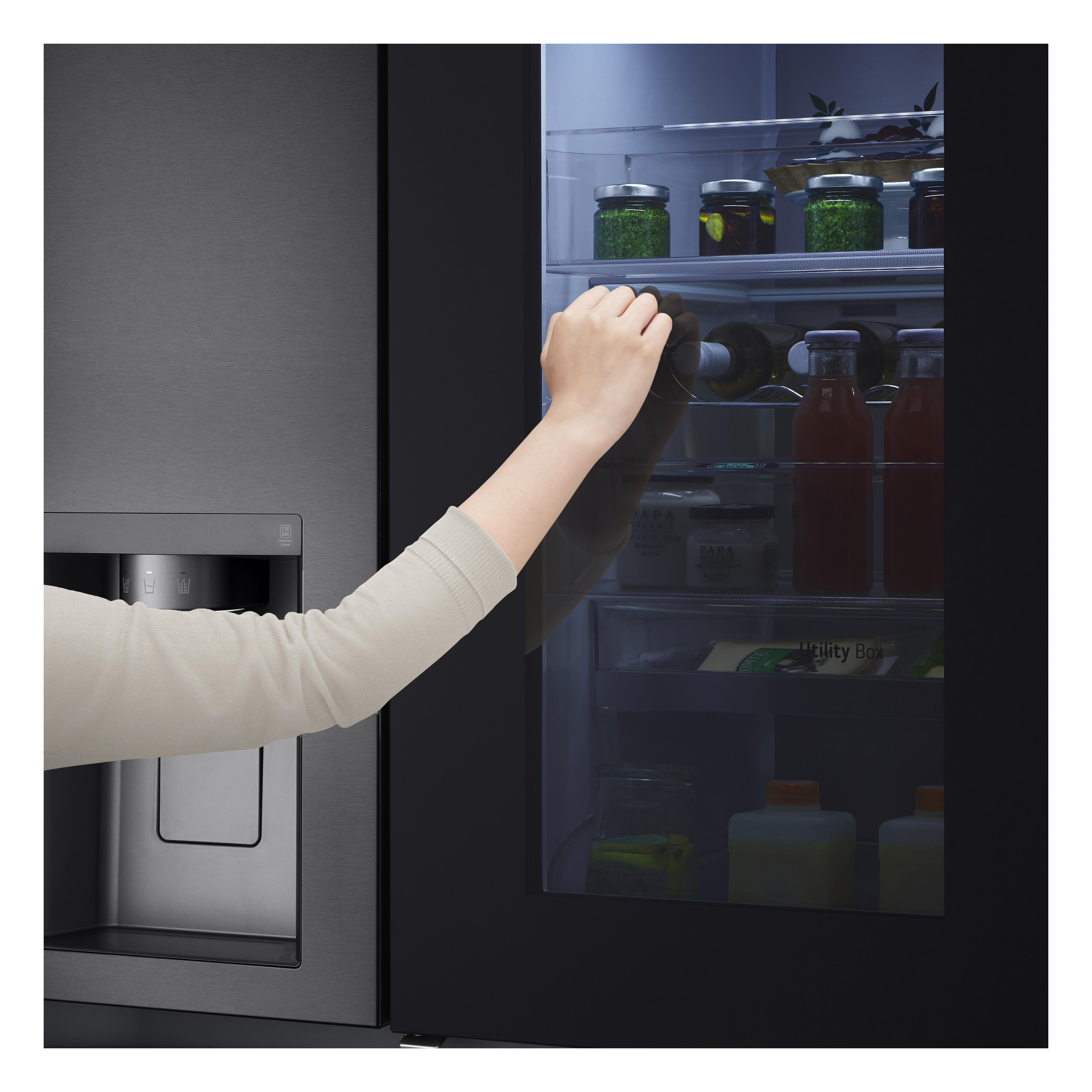 Eine Hand greift in einen Kühlschrank mit dunklem Innenraum. Flaschen und Gläser sind innen sichtbar.