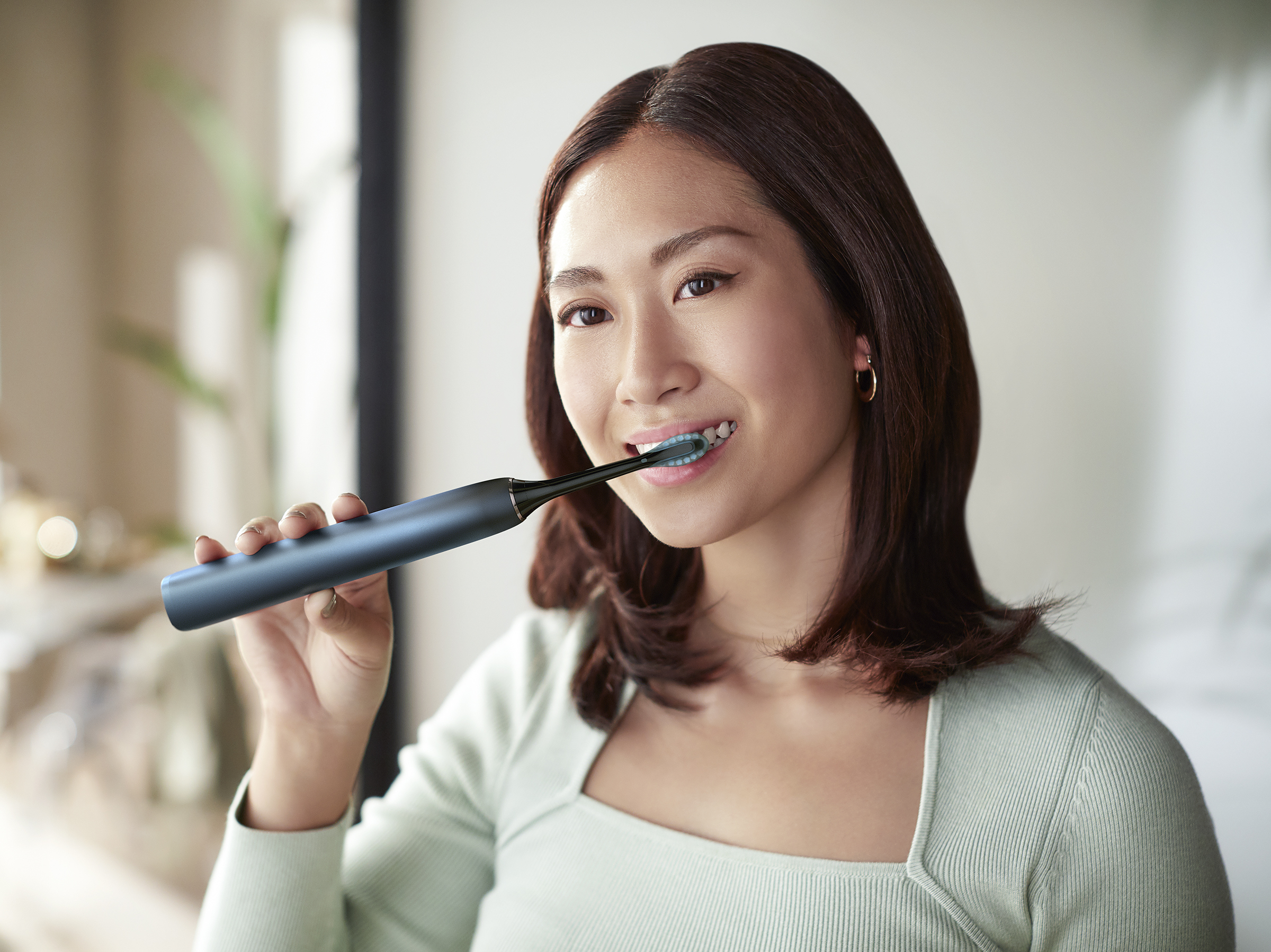 Femme se brossant les dents avec une brosse à dents électrique bleue dans la salle de bain.