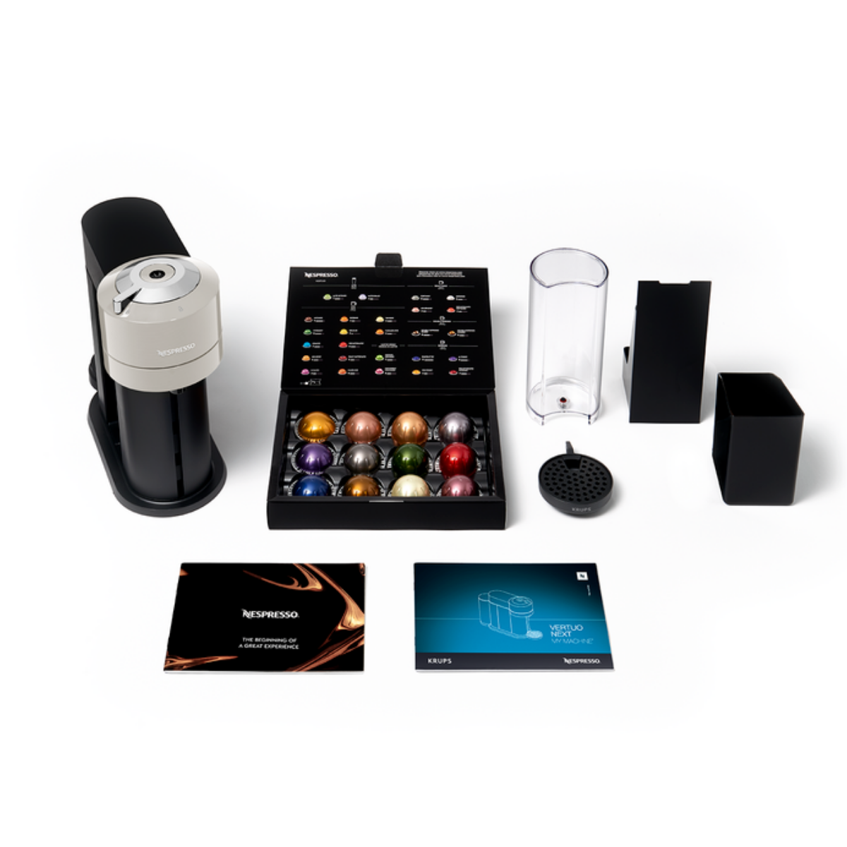Máquina Nespresso con cápsulas, accesorios e instrucciones. Colores negro y plata. Fondo blanco.