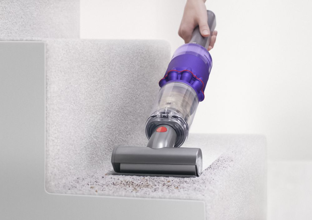 Una persona aspirando una escalera alfombrada con una aspiradora morada y gris.