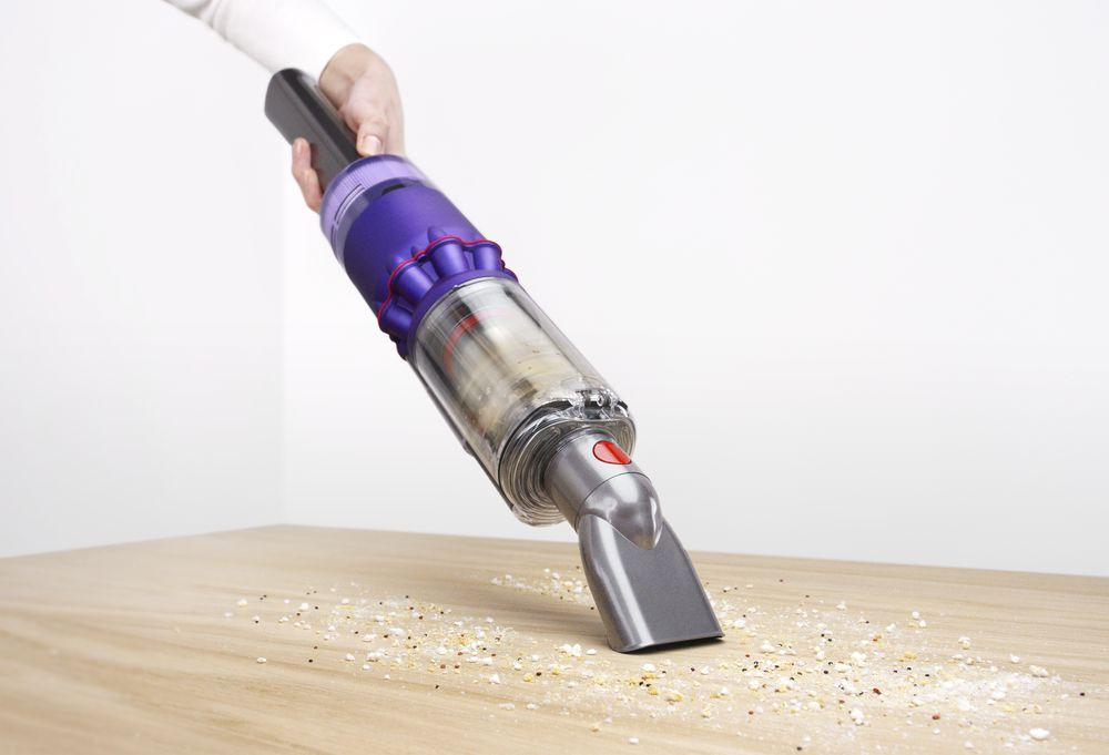 Persona limpiando una mesa de madera con una aspiradora de mano Dyson. Aspirando migas.