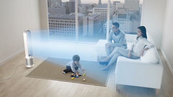 Un ventilador Dyson soplando aire hacia una familia sentada en un sofá. Un niño juega.