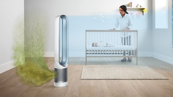 Una habitación con un purificador de aire blanco, una cuna y una mujer de pie cerca de la cuna.
