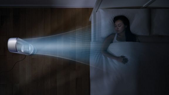 Una mujer durmiendo en la cama con un ventilador soplando aire, vista superior, suelo de madera.