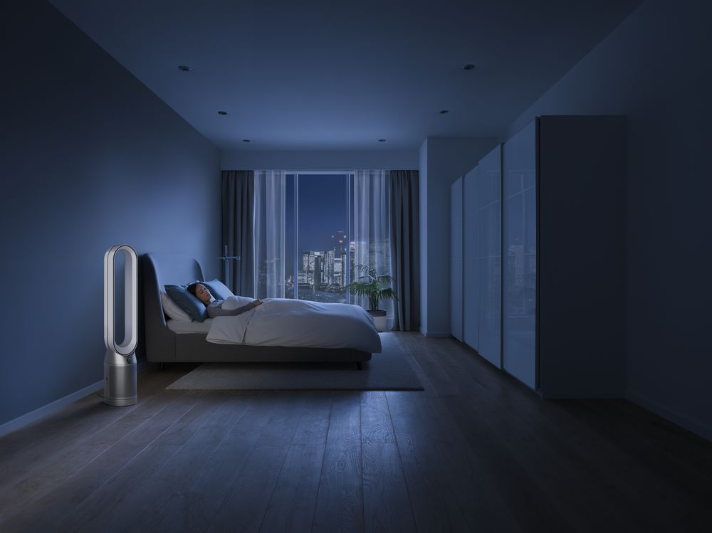 Una persona durmiendo en la cama junto a un purificador de aire.