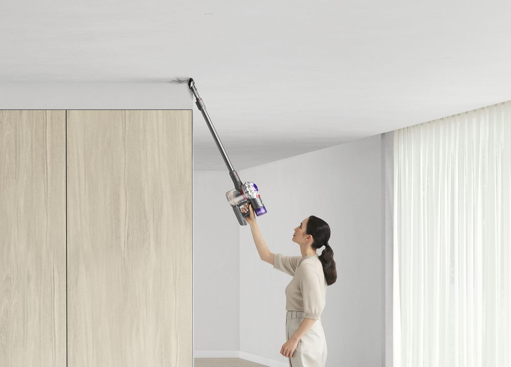 Mujer aspirando un techo con una aspiradora inalámbrica, cerca de un armario de madera.