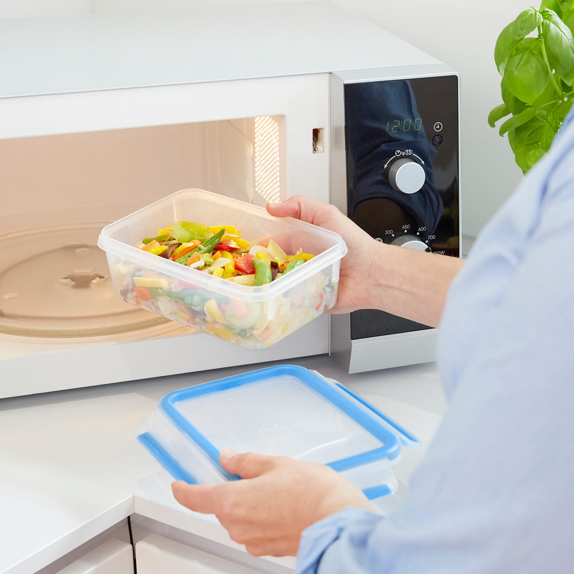 Una persona sacando un recipiente de verduras del microondas. Otro recipiente.
