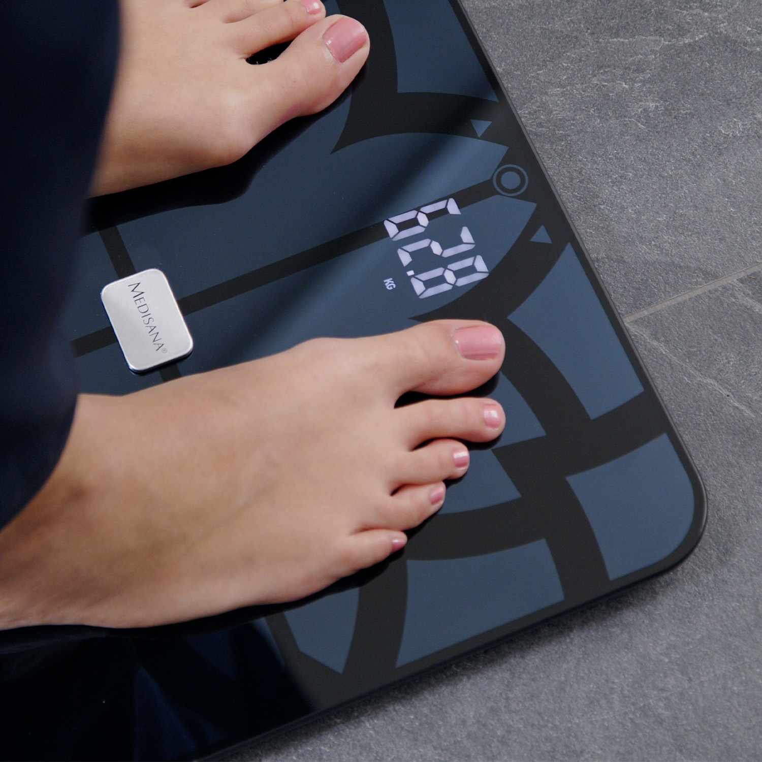 Füße auf einer Digitalwaage. Das Display zeigt ein Gewicht in Kilogramm an.