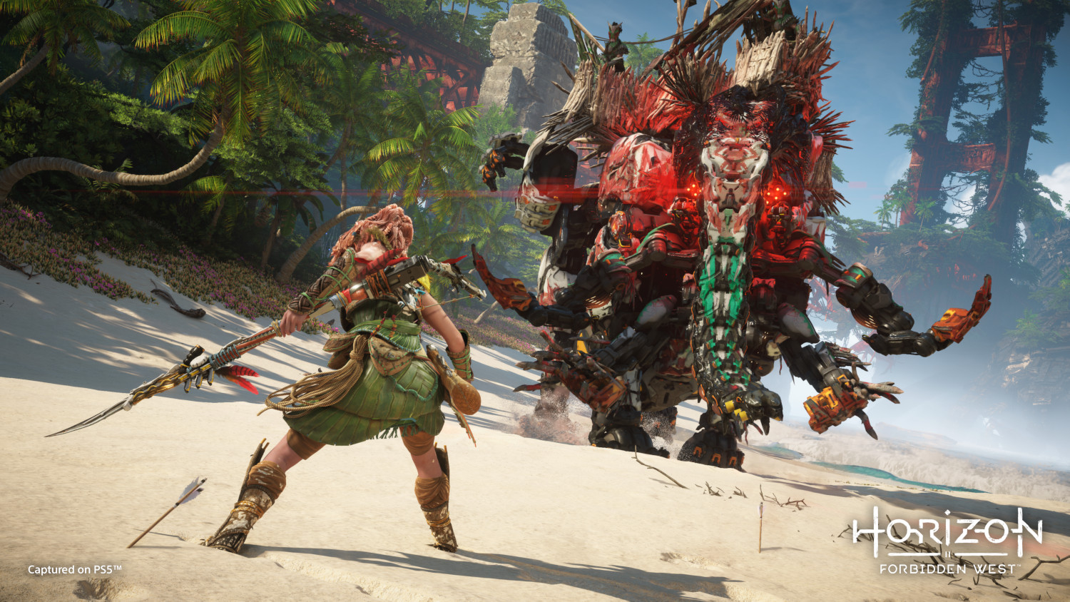 A woman with a spear faces a large red robot on a sandy beach.