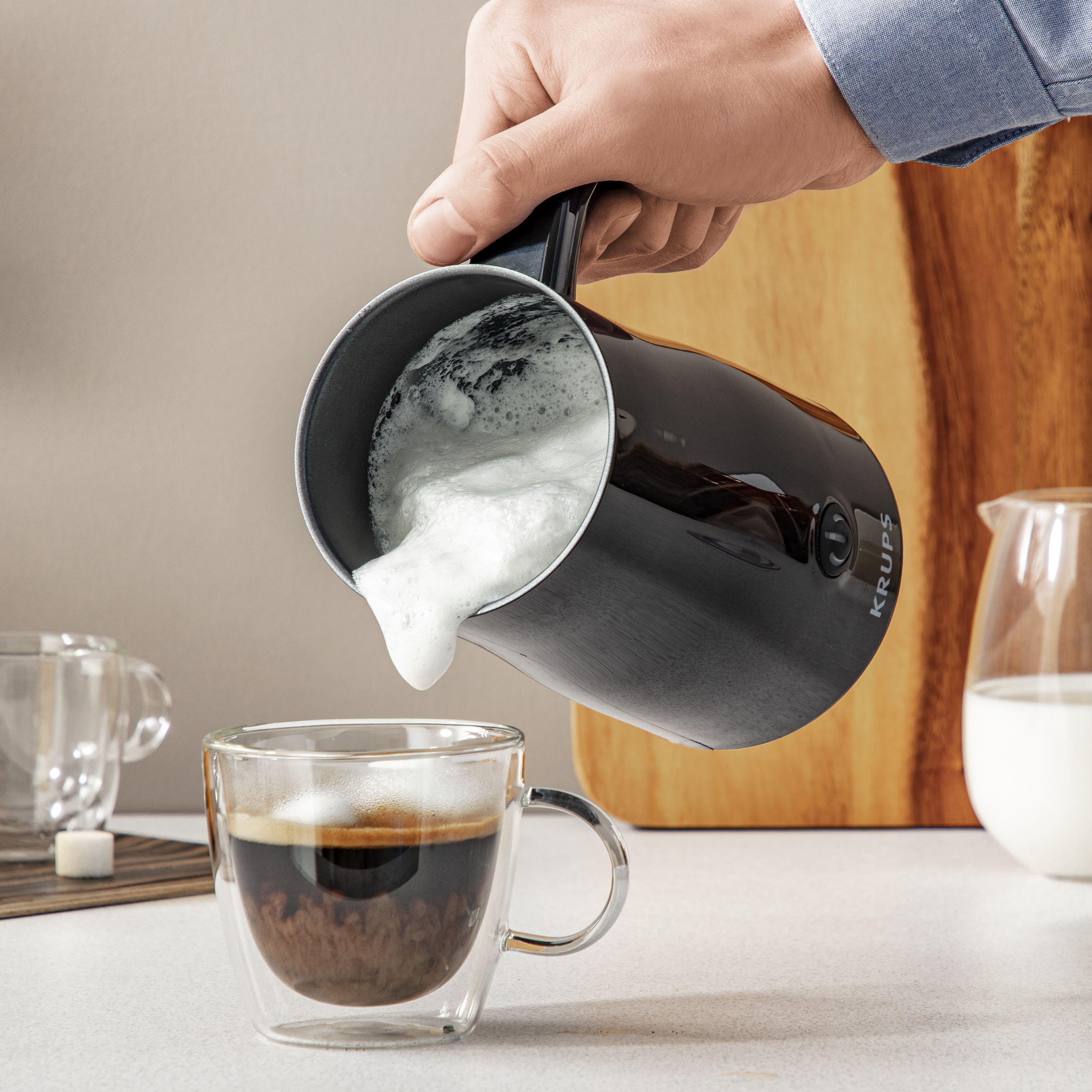 Una mano vierte espuma de un espumador de leche negro en un vaso de café.