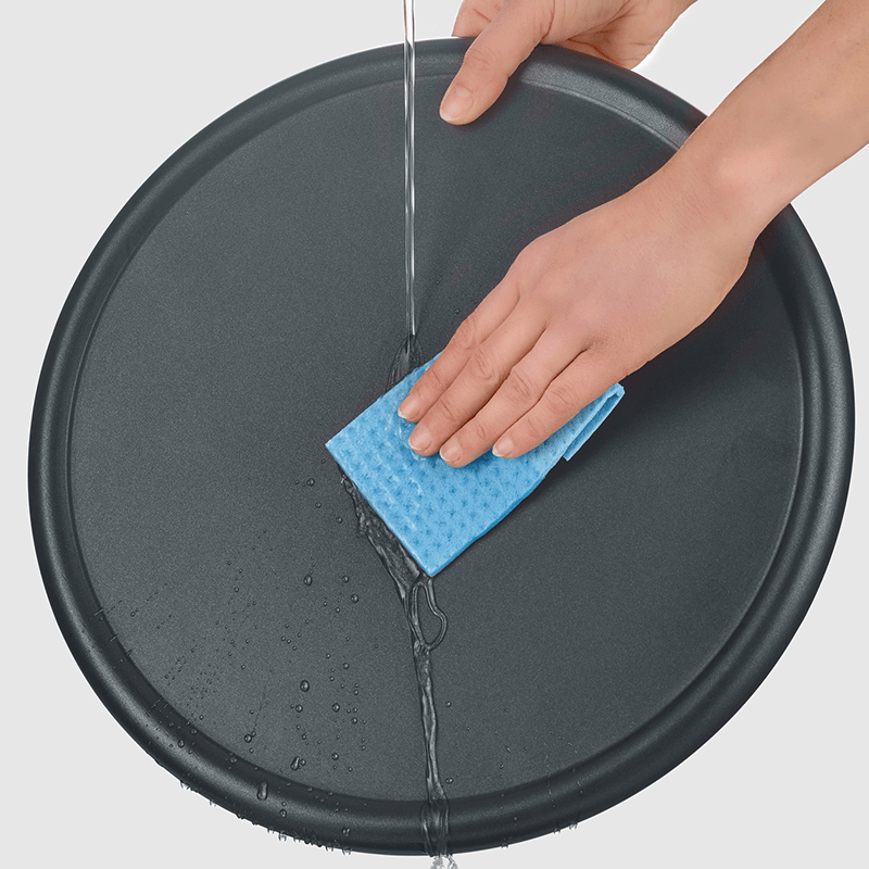 Eine Hand spült eine dunkle, runde Pfanne mit einem blauen Schwamm aus.