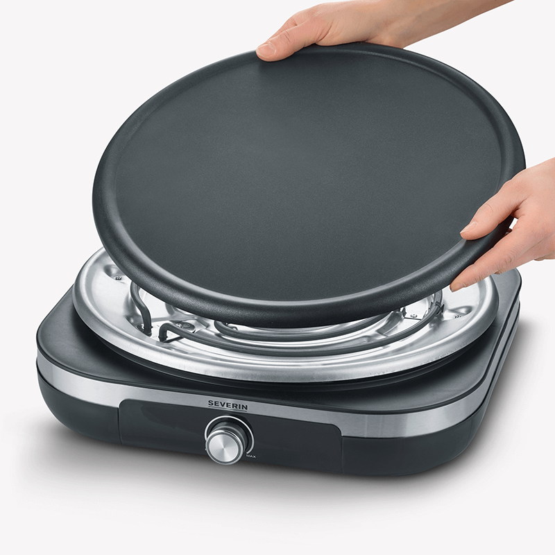 Hände halten eine Grillplatte über einem Grill. Silberne Basis mit Drehknopf.
