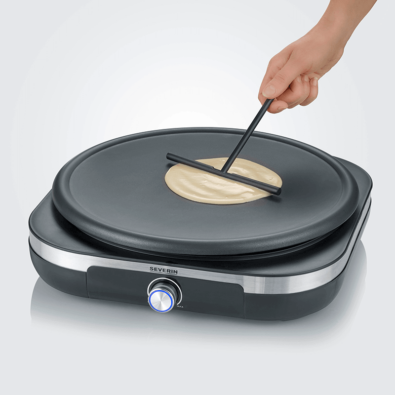 Person benutzt Teigverteiler auf Crêpes-Maker, Pfannkuchen auf der Oberfläche.