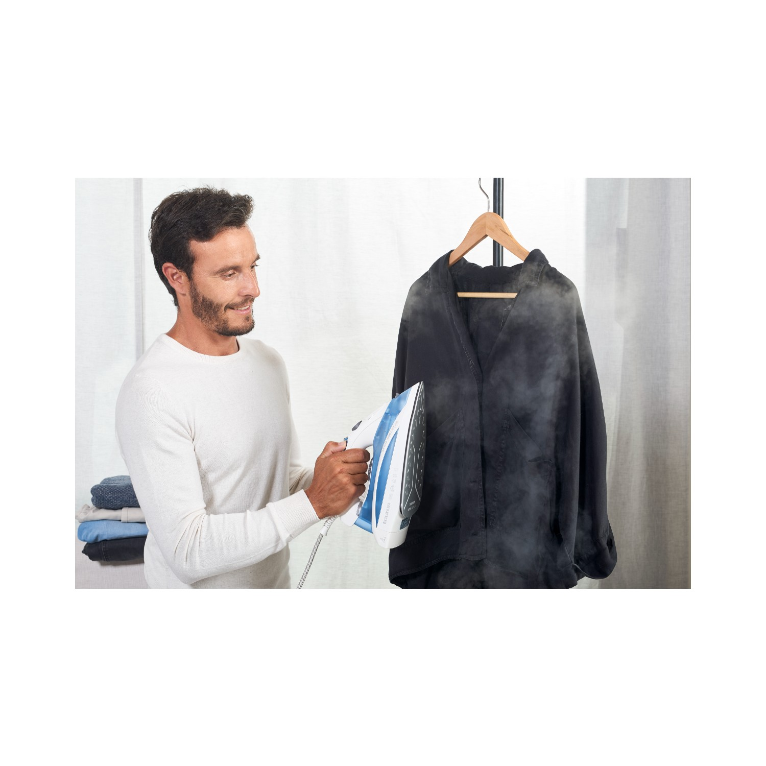 Un hombre planchando una chaqueta negra. Sale vapor. Ropa en una percha.