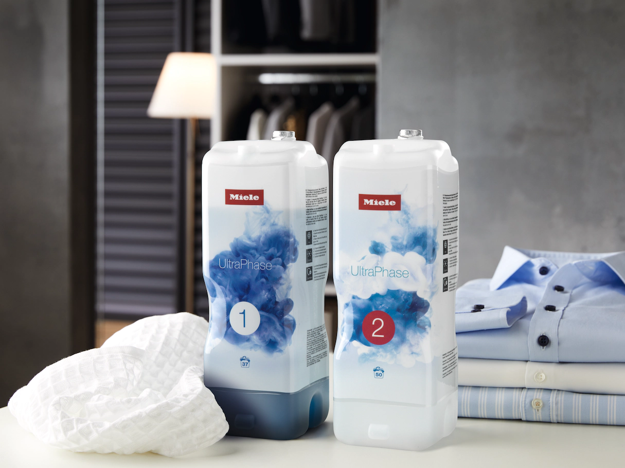 Deux bouteilles de détergent Miele UltraPhase. Étiquettes blanches et bleues, placées sur une étagère grise.