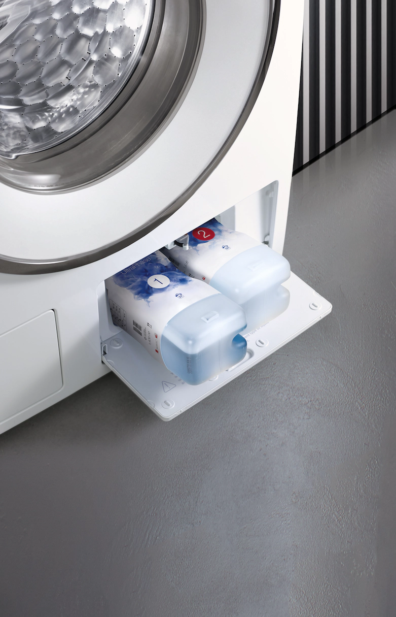 Un lave-linge avec des récipients de détergent visibles. La machine est de couleur blanche.