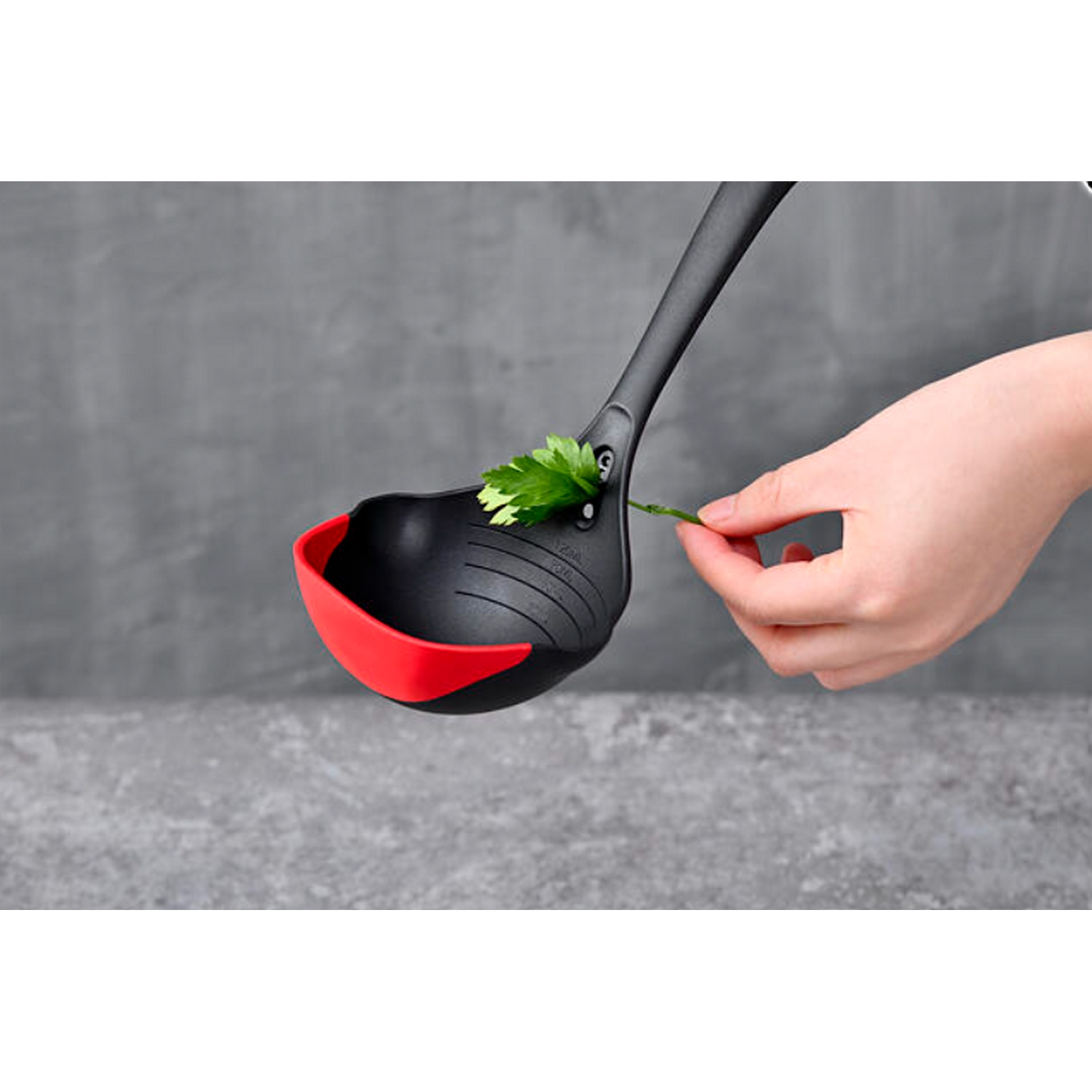 Un cucharón negro y rojo con una hoja verde, con una mano sosteniendo un tallo.