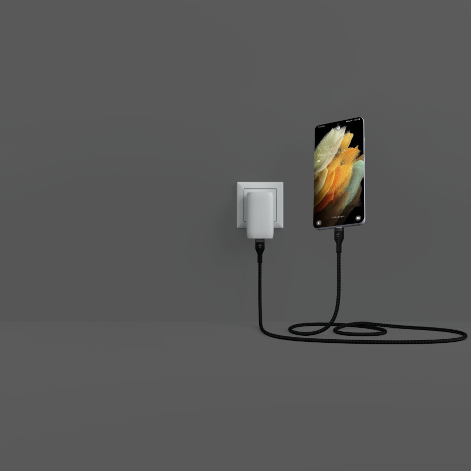Un smartphone se recharge avec un câble. Le téléphone est branché sur un chargeur mural. Le fond est gris.
