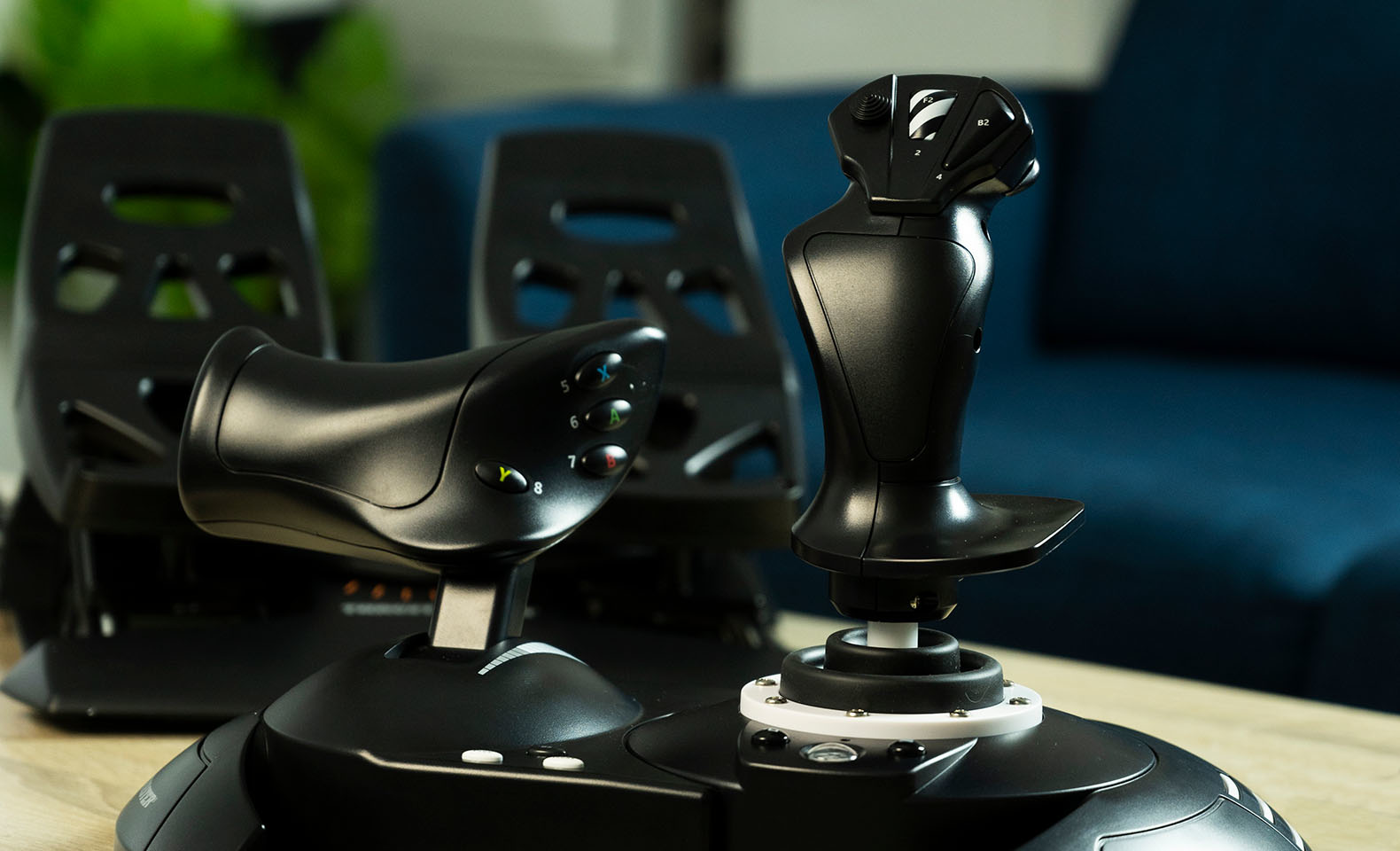 Joystick nero per simulatore di volo. Due controller su un tavolo di legno. Divano blu sullo sfondo.