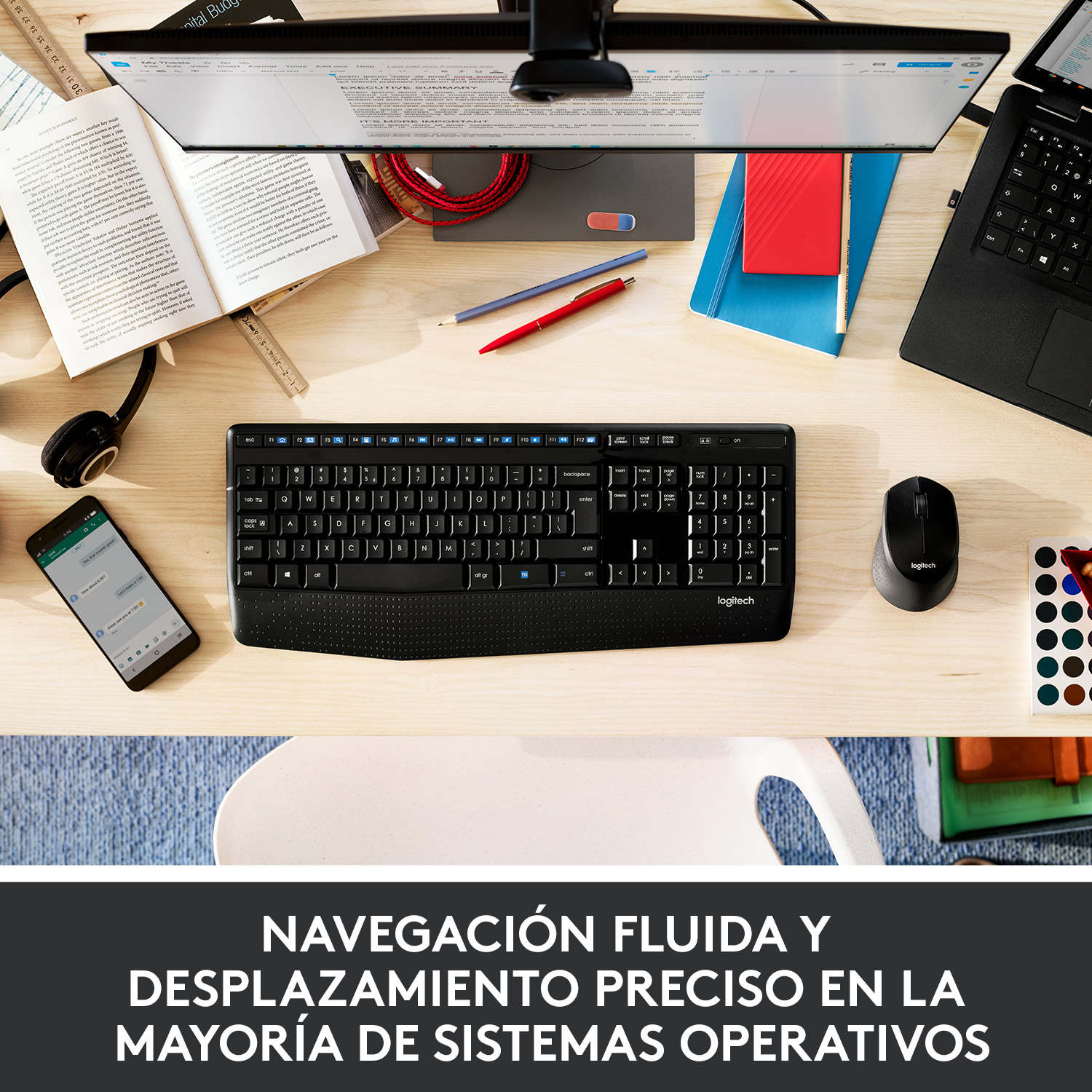 Configuración de escritorio: teclado, ratón, monitor, teléfono, libro rojo y otros objetos en escritorio de madera.