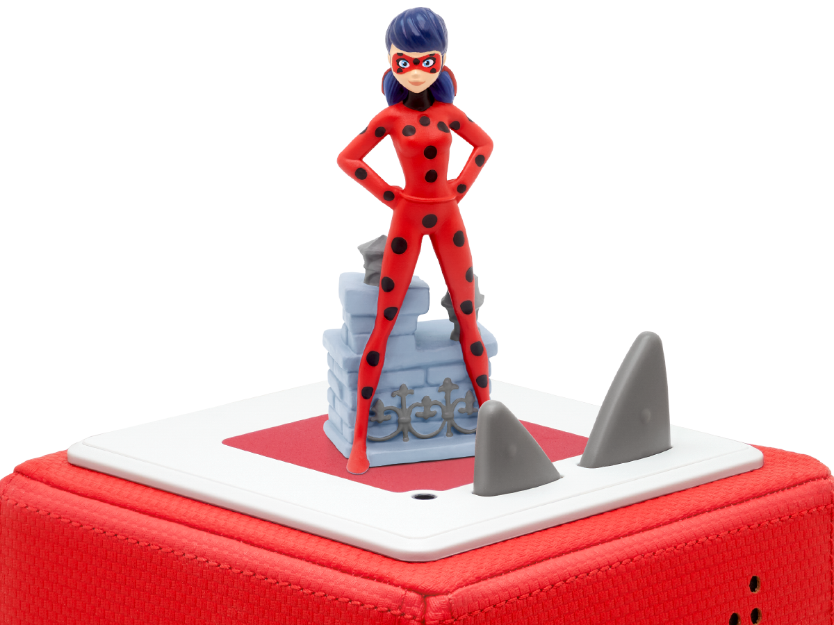 Marienkäfer-Figur, die auf einer Box mit Haifischflossen-Dekor steht. Schwarzer Hintergrund.