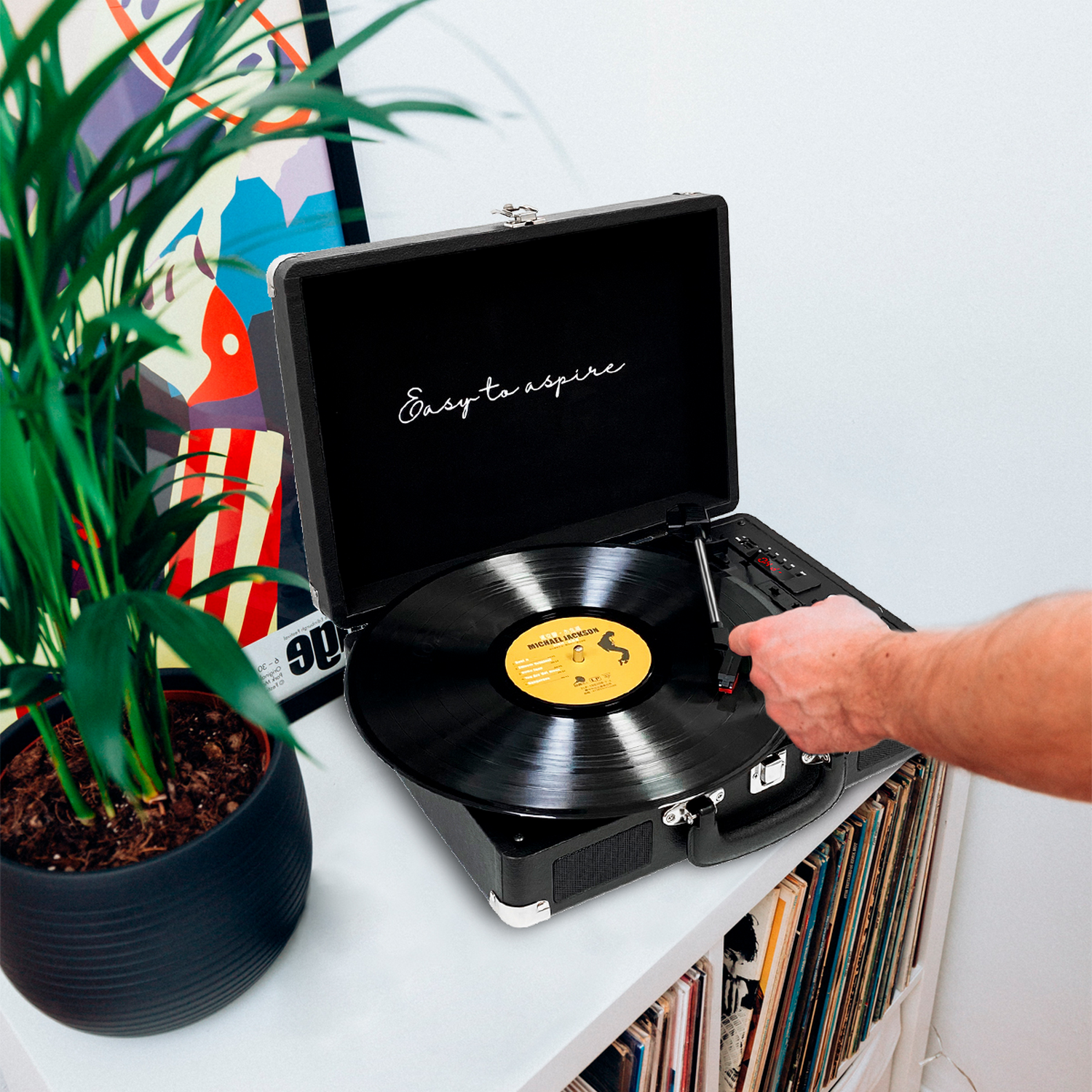 Persona poniendo un disco en un tocadiscos. Una planta en el fondo.