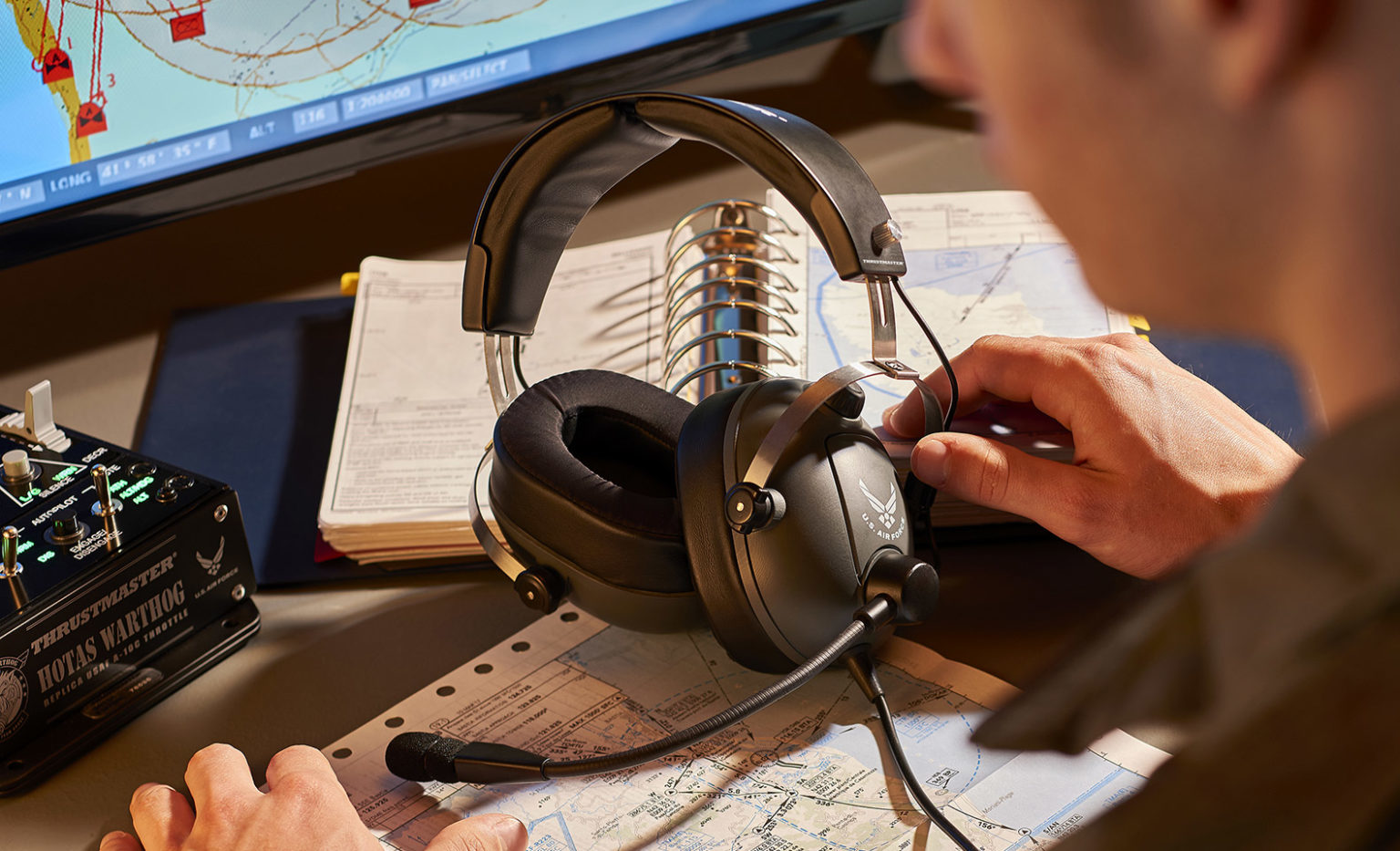 Ein Pilot sitzt an einem Tisch mit Kopfhörern, Karten, Dokumenten und einem Flugsimulator-Bedienfeld.