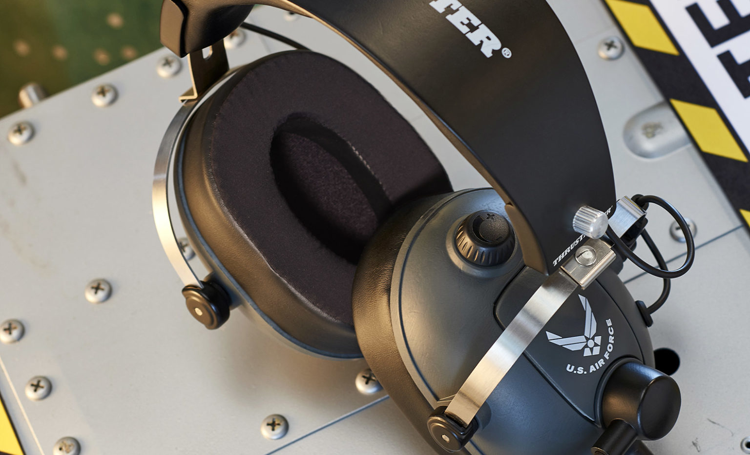 Nahaufnahme eines schwarzen Luftfahrt-Headsets mit US-Luftwaffen-Logo auf metallischer Schraubfläche.