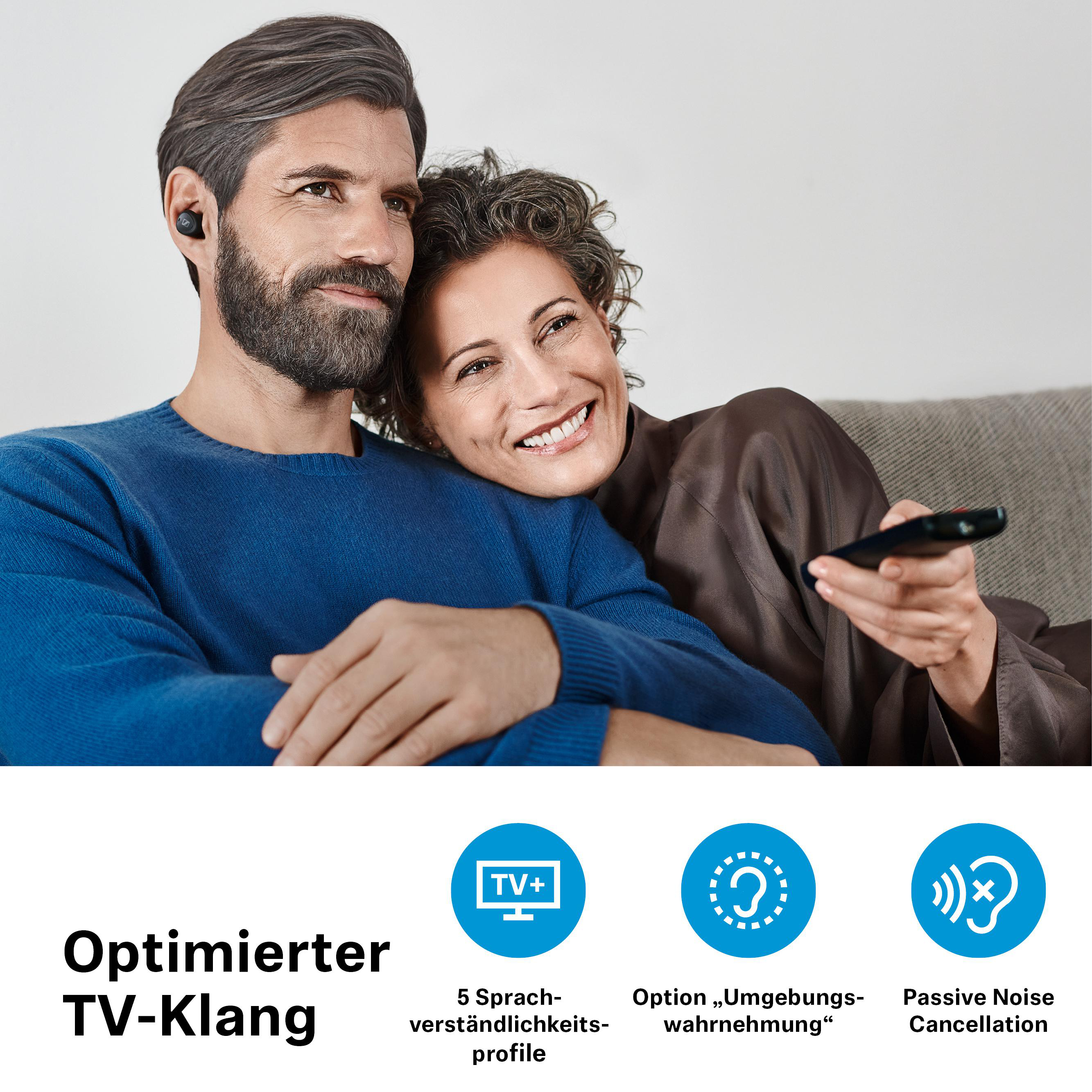Ein Paar auf einem Sofa, einer trägt Ohrhörer und hält eine Fernbedienung.