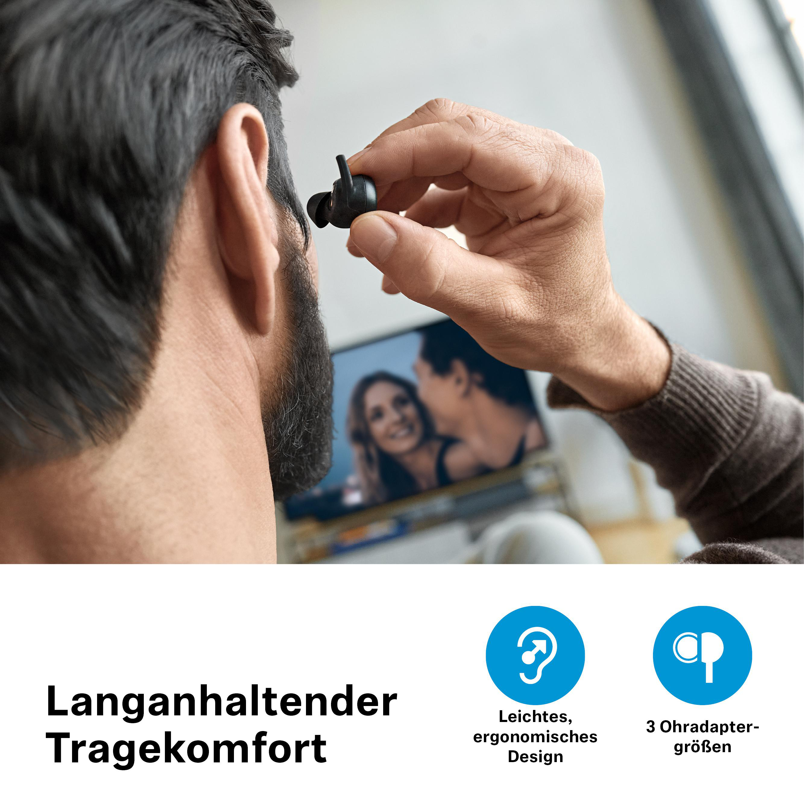 Ein Mann mit Bart trägt schwarze Ohrhörer, im Hintergrund ein Fernseher.