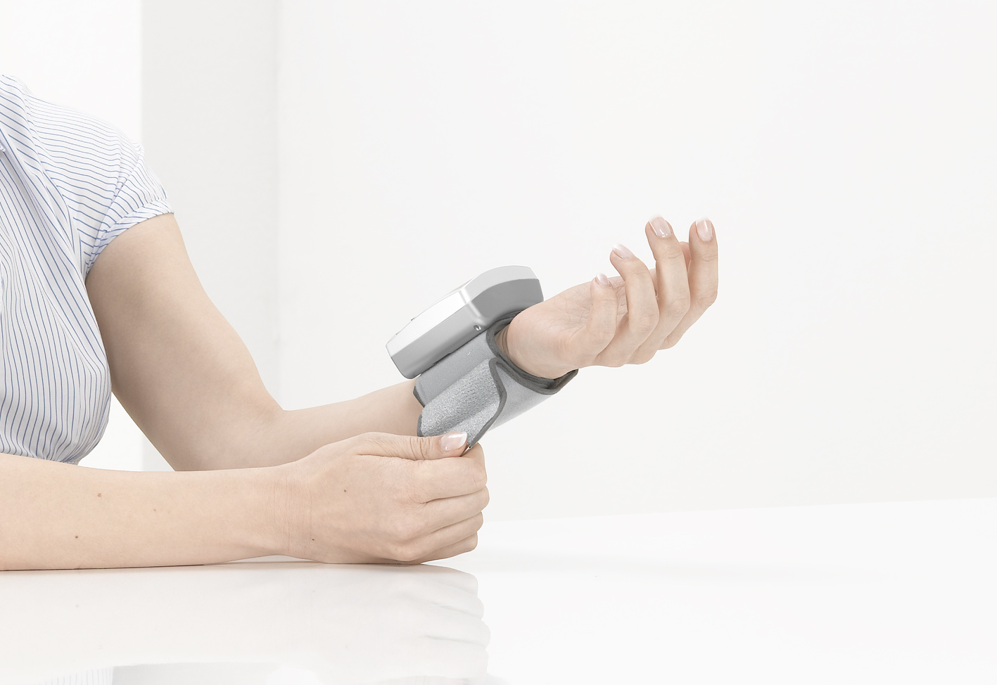 Person mit Blutdruckmessgerät am Handgelenk. Weißer Hintergrund mit weißem Tisch.
