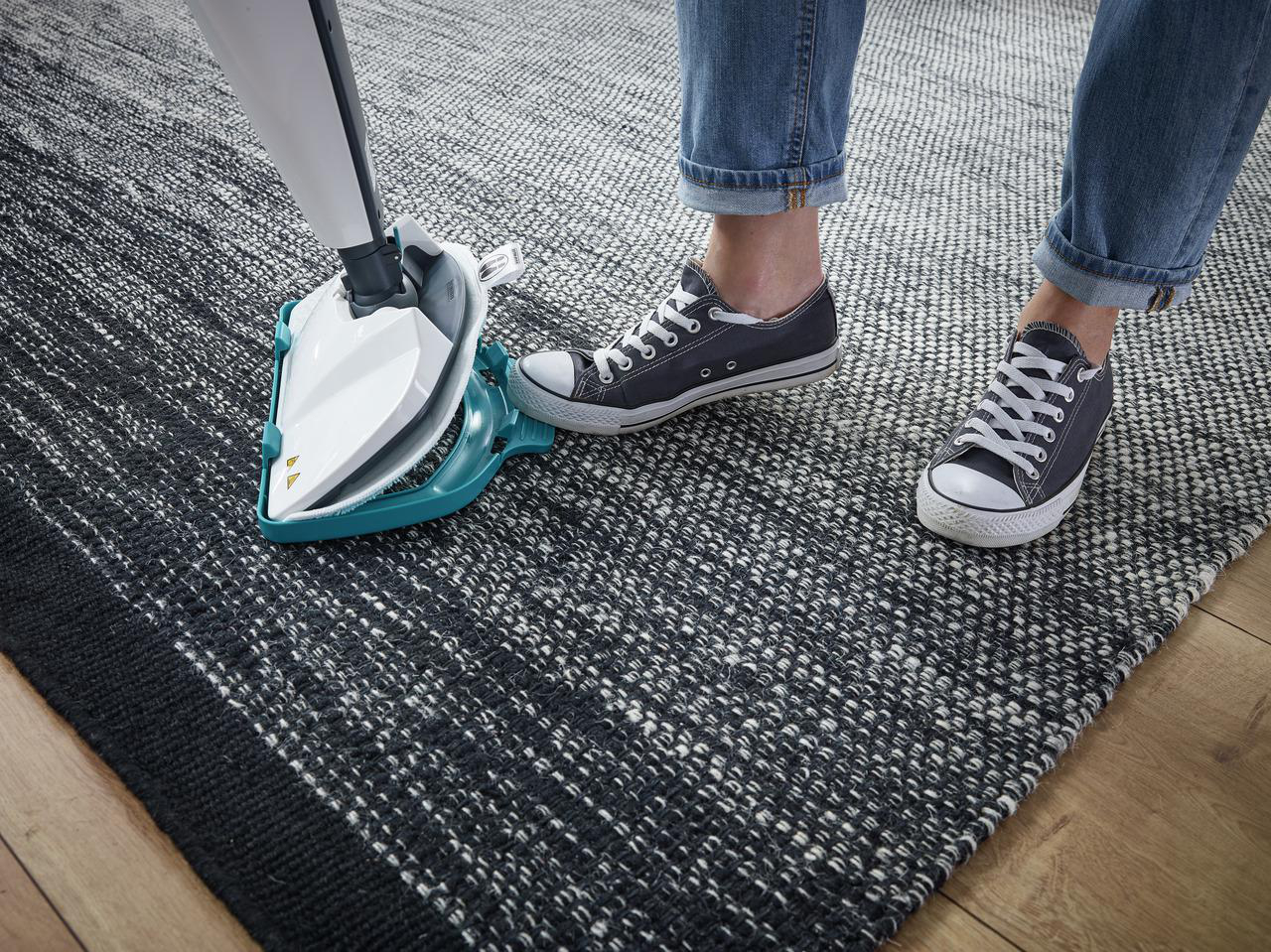 Eine Person reinigt einen Teppich mit einem Dampfreiniger. Der Teppich ist schwarz-weiß.