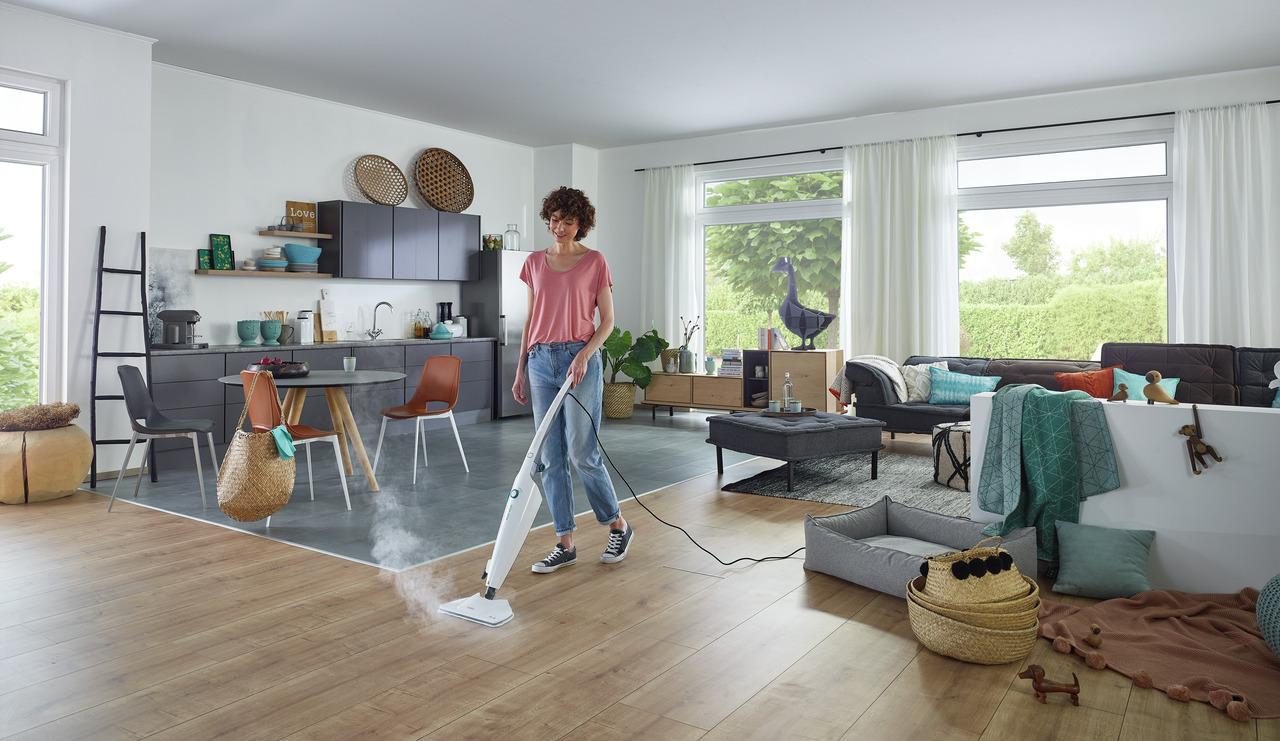 Frau reinigt Holzboden mit Dampfreiniger in einem Wohnzimmer.