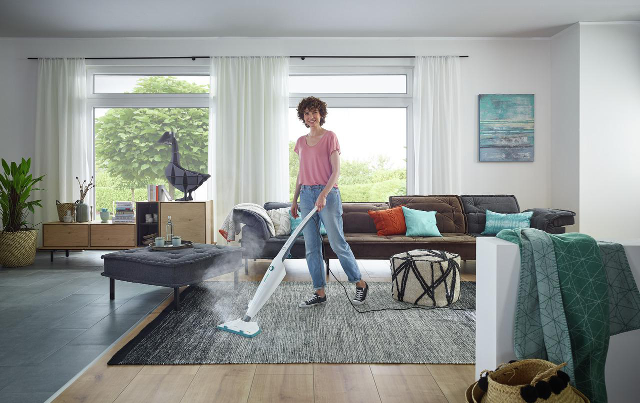 Eine Frau reinigt einen Teppich mit einem Dampfreiniger in einem modernen Wohnzimmer.
